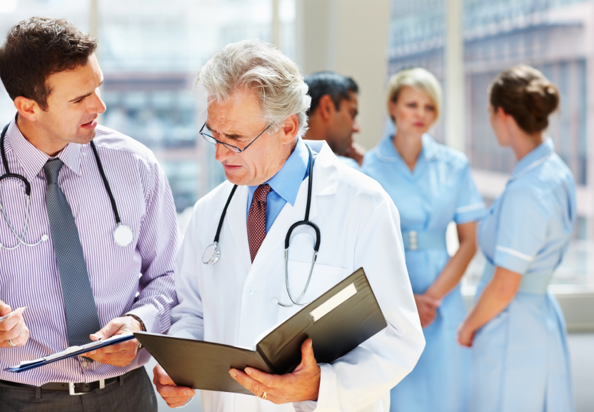 Portrait of two doctors discussing schedule while their team in background